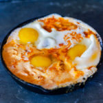 cast iron skillet with eggs simmering in a tomato crema sauce.
