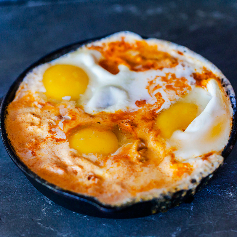 cast iron skillet with eggs simmering in a tomato crema sauce.