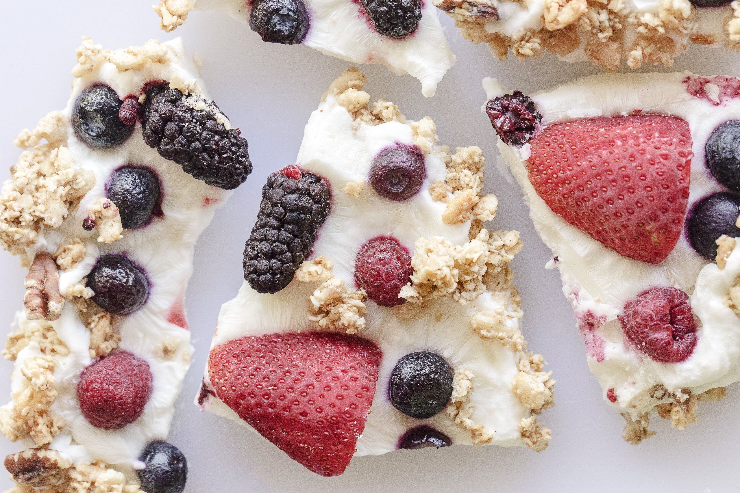 pieces of frozen white yogurt bark with berries and granola on