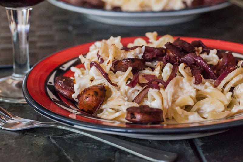 red wine simmered sausages served over a platter of creamy cheesy noodles