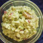 chunky avocado guacamole with tomato, cheese and serrano chile in a glass bowl