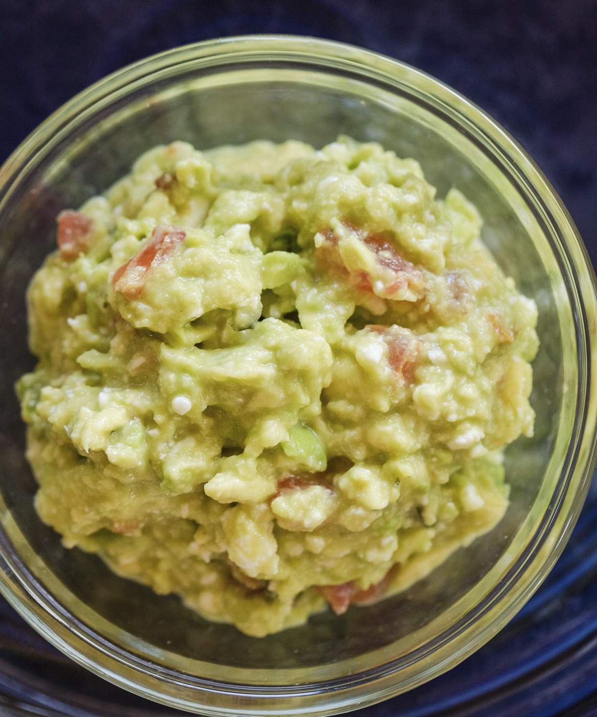 chunky avocado guacamole with tomato, cheese and serrano chile in a glass bowl