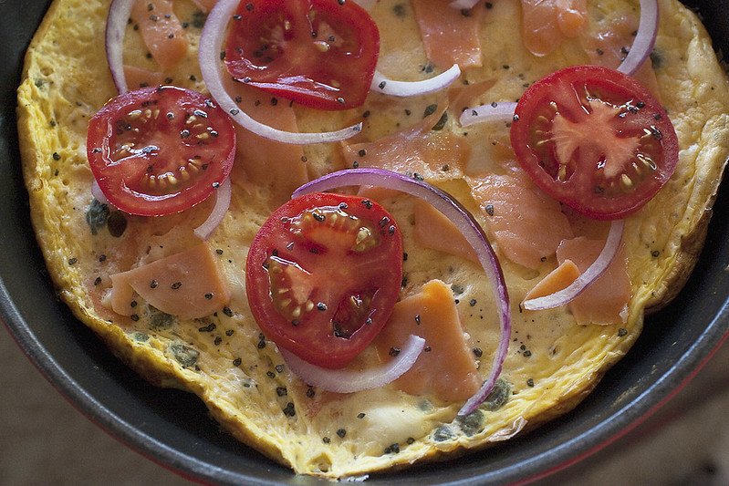 campari tomatoes, lox, red onion and herbs on top of a cream cheese frittata