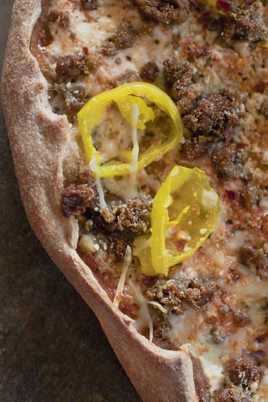 close up photo of a slice of thin crust pizza with yellow peppers and vegetarian sausage
