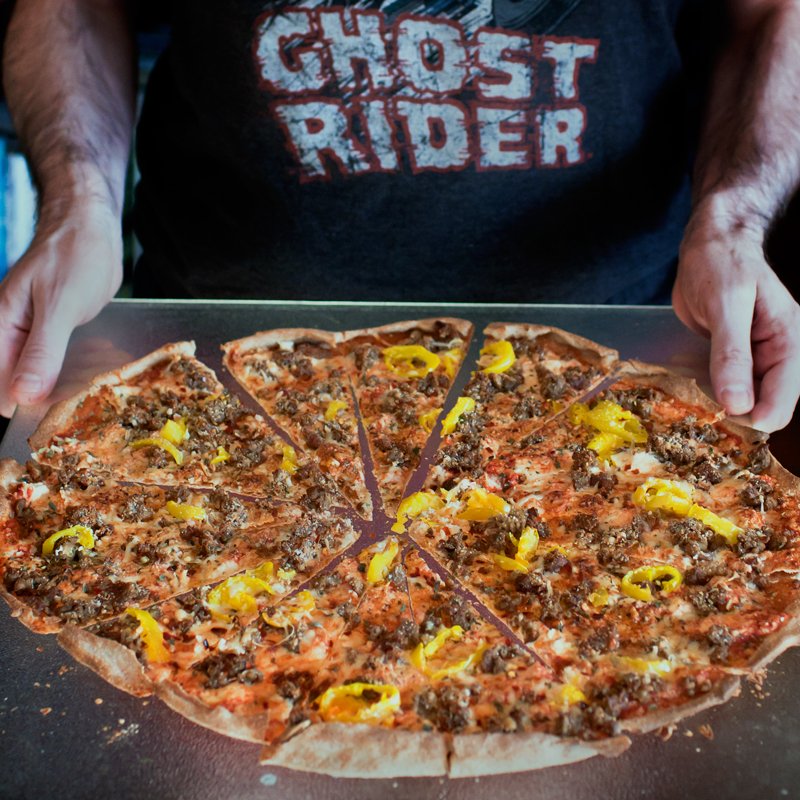 man in a ghost rider shirt holding tray of homemade pizza