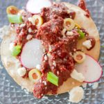 Vegan Sonoran tostada topped with crispy tofu tossed in red chile sauce, radishes, green onion and olives