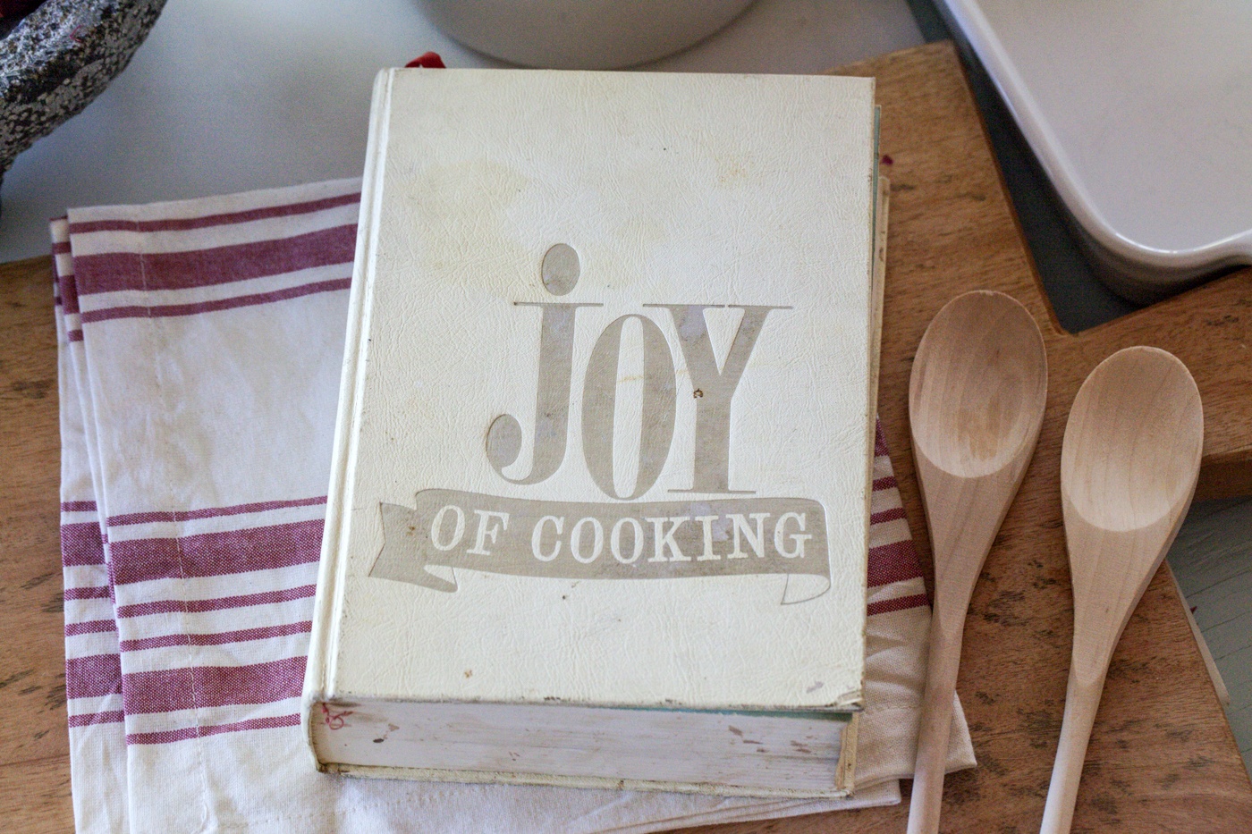 Vintage edition of Joy of Cooking on a kitchen table with wooden spoons