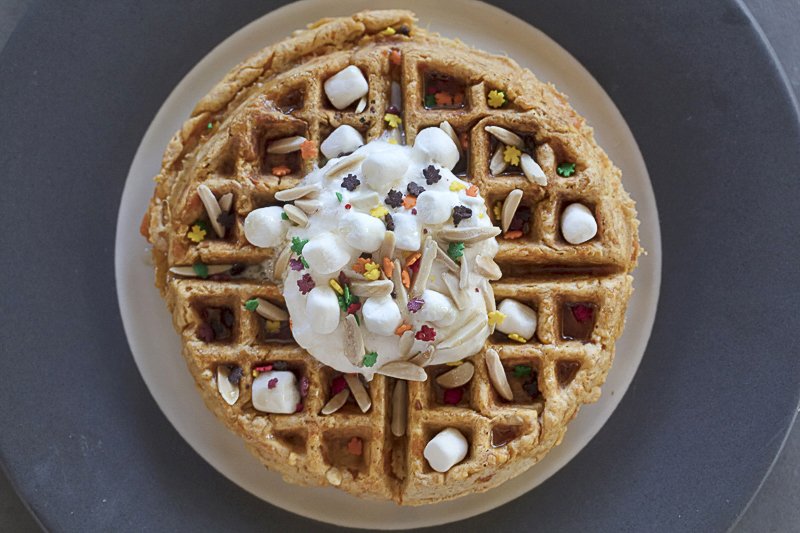 sweet potato waffle topped with whipped cream, mini marshmallows, sprinkles and almonds