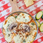 layered lasagna dip topped with melted mozzarella, herbs and mushroom slides