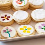 white fondant circles on sugar cookies with hand painted flowers on a parchment lined baking sheet