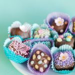 chocolate dipped brownie bites decorated with different kinds of pastel sprinkles served in paper liners to look like boxed chocolates