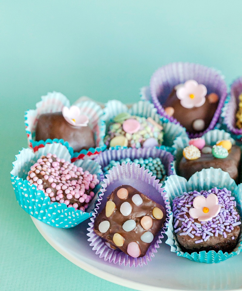 chocolate dipped brownie bites decorated with different kinds of pastel sprinkles served in paper liners to look like boxed chocolates