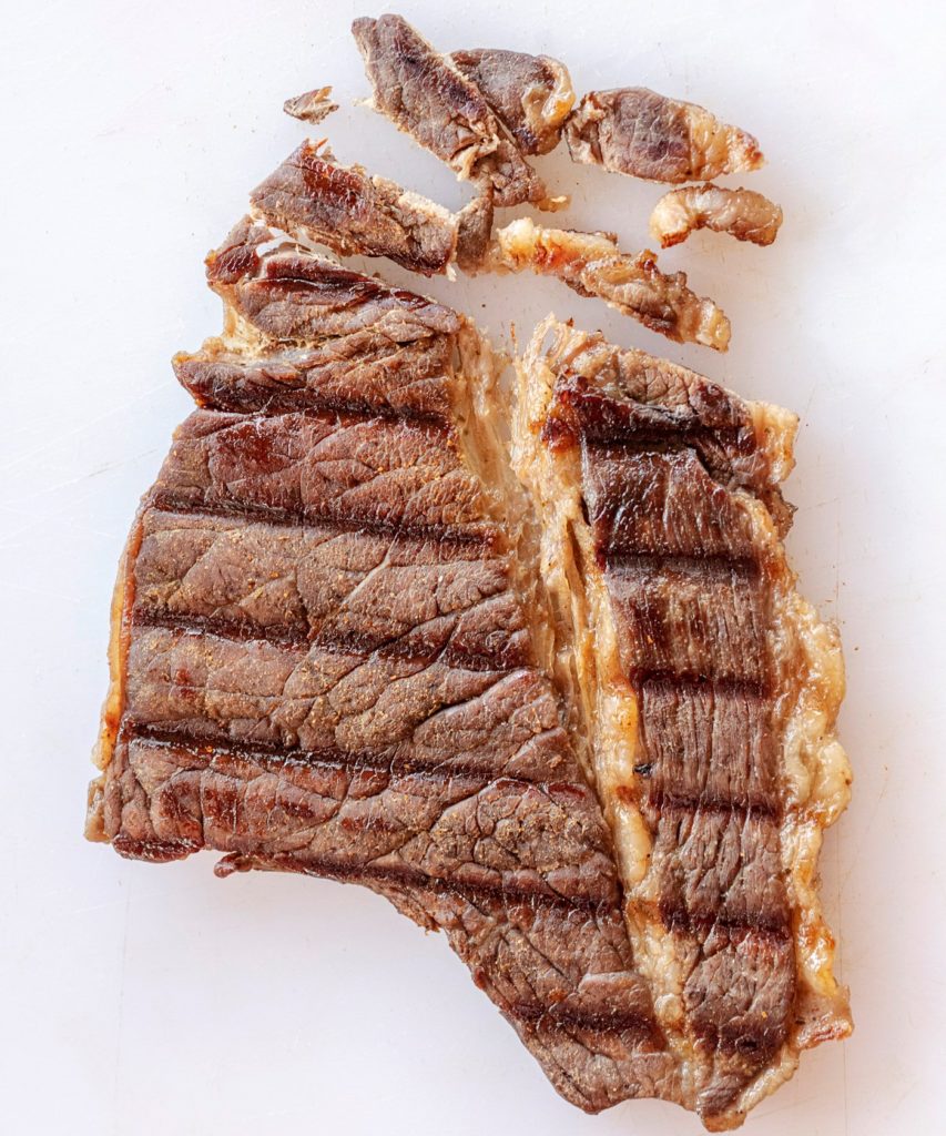 Bottom Round steak on a white cutting board, grilled for carne asada showing how to slice the meat against the grain.