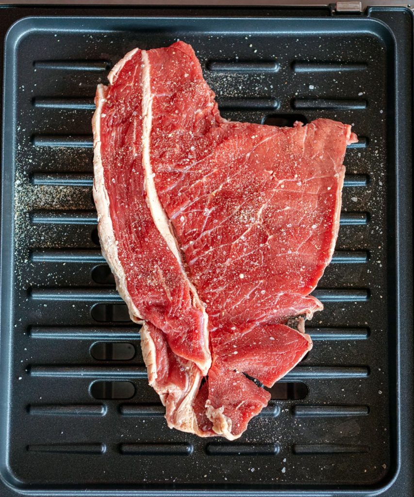 Bright red raw Bottom Round steak seasoned with salt, chile powder and Mexican oregano placed on a George Foreman Grill