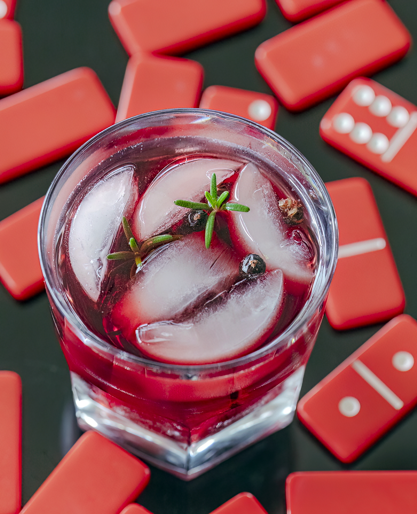 a bright red whisky cocktail surrounded by red dominos