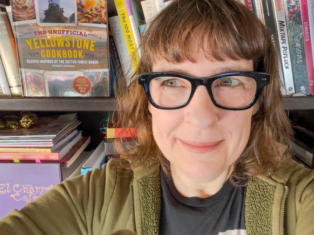 self portrait of author Jackie Alpers with cookbooks
