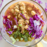 bowl of Sonoran style red pozole with pork, hominy, citrus, chiles, red cabbage and green onions