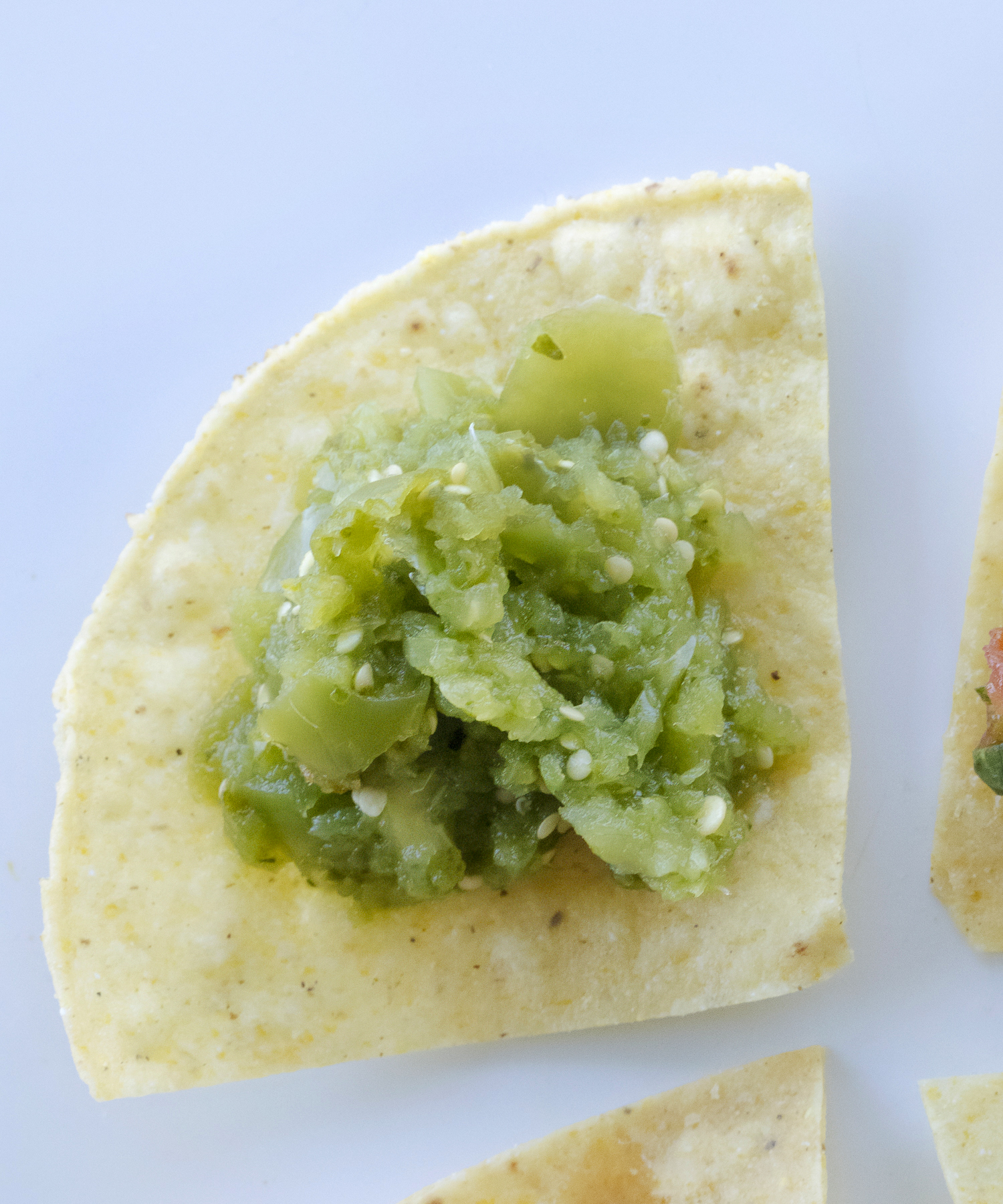 Green tomatillo salsa served on a corn tortillas chip on a bright white background