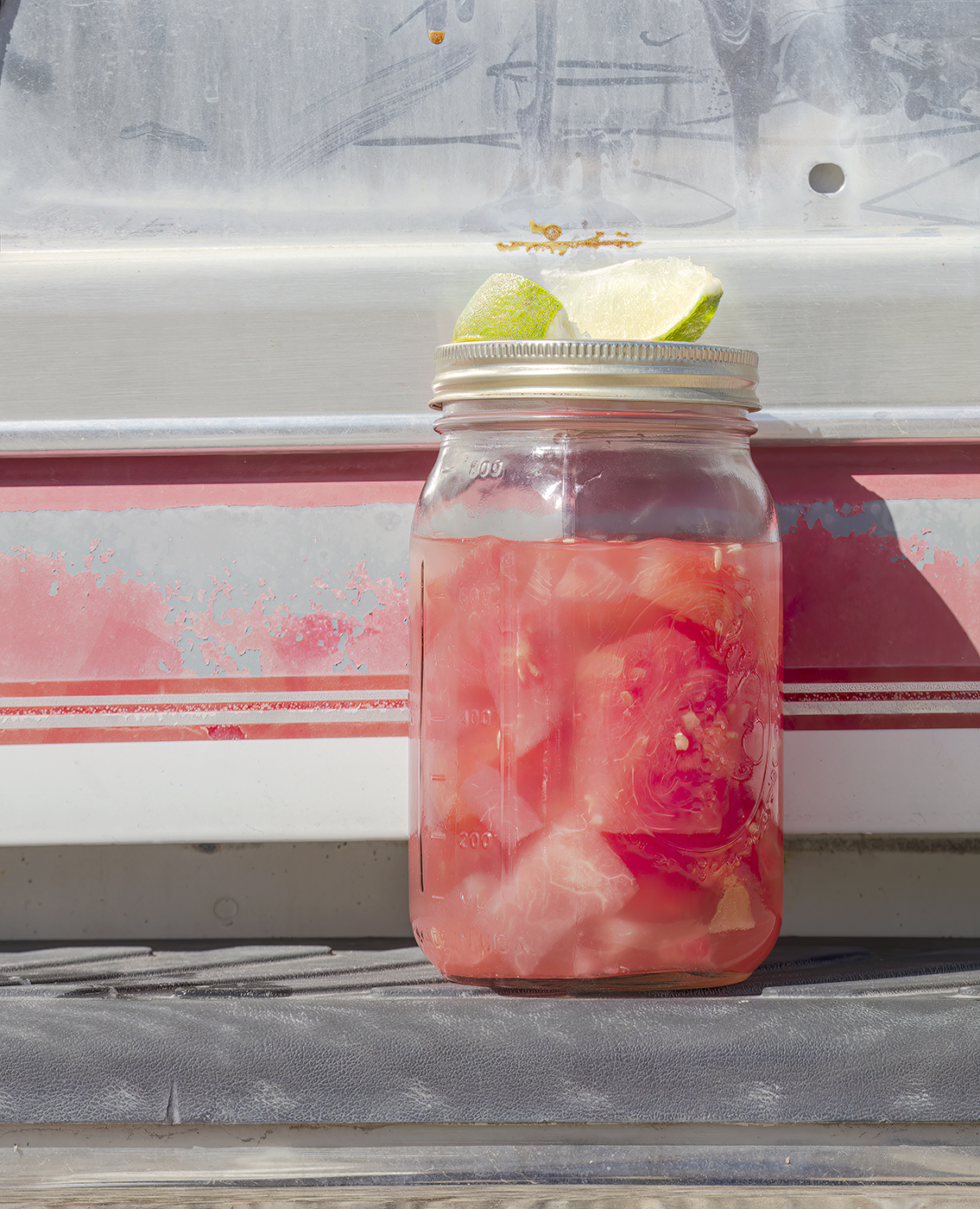 Watermelon moonshine in a bell jar on the back of a pickup truck. Served with lime to cut the burn.