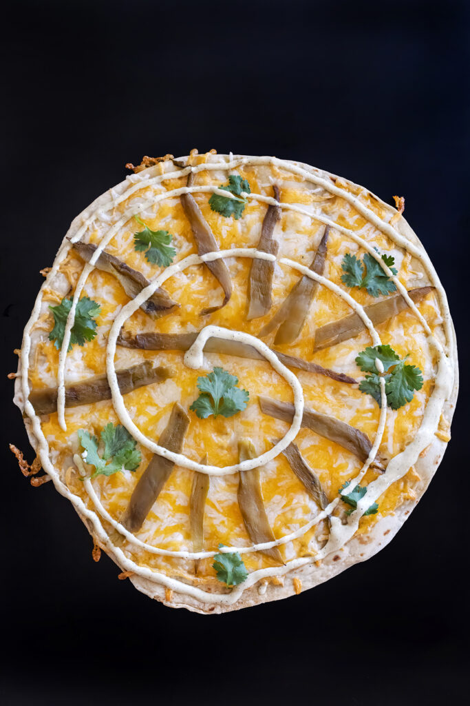 Sonoran style Arizona style Southwestern flour tortilla cheese crisp with Mexican blend cheese roasted green chile strip, cilantro leaves and ranch spiral.