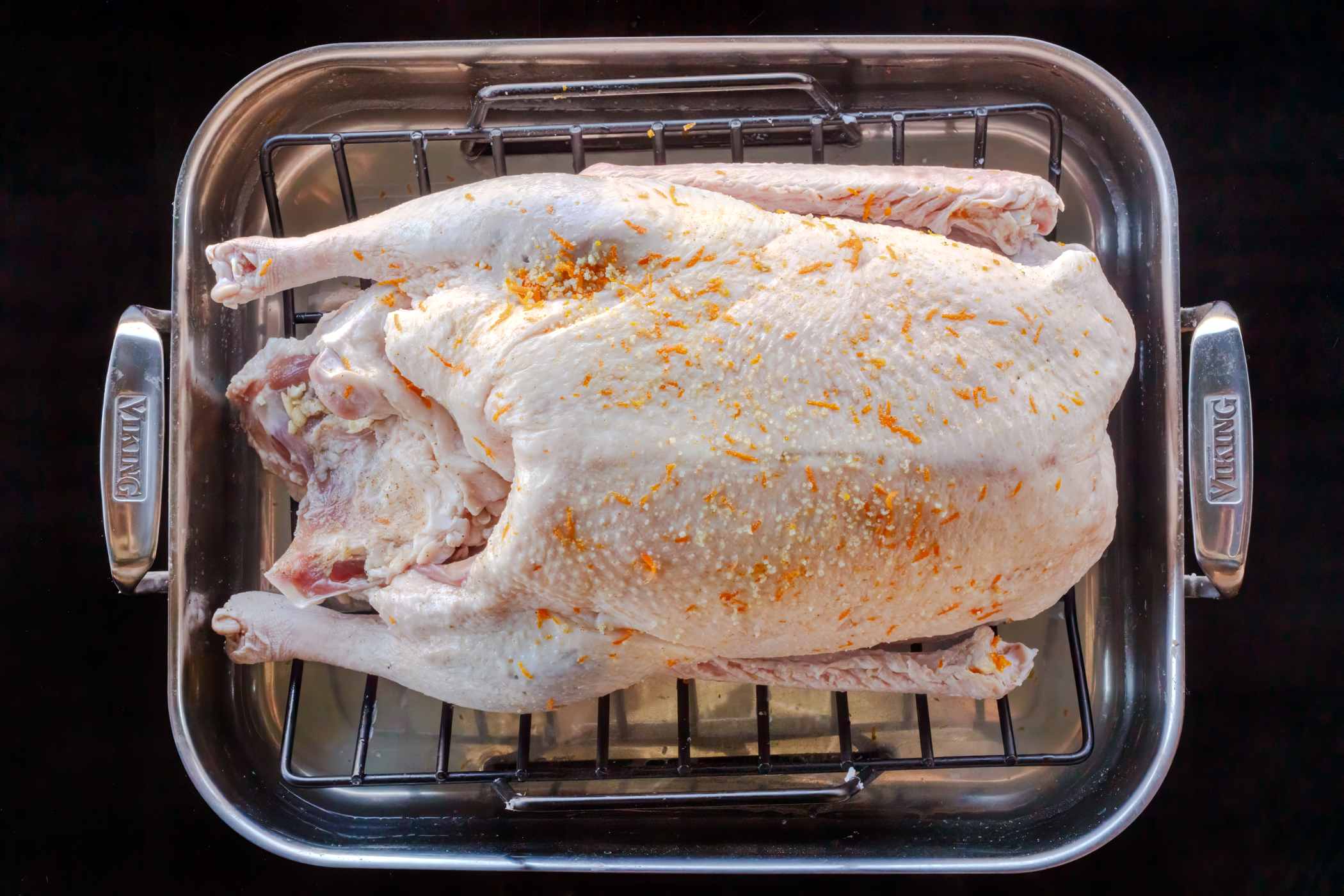 Raw roast goose with orange and salt rub in a Viking roasting pan with insert on a black background.