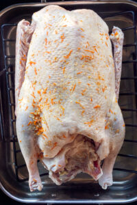 Raw roast goose with orange and salt rub in a Viking roasting pan with insert on a black background.