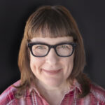 Portrait of food photographer and cookbook author Jackie Alpers 2025, square format, black background, red plaid shirt in Tucson Arizona