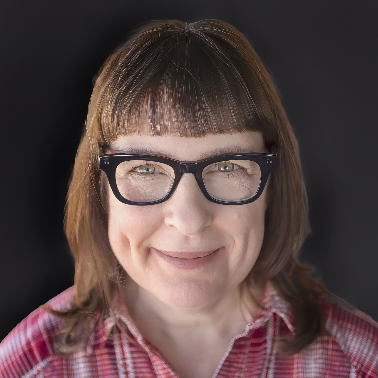Jackie-Alpers-portrait-2025 Portrait of food photographer and cookbook author Jackie Alpers 2025, square format, black background, red plaid shirt in Tucson Arizona