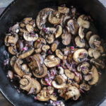 Recipe photography of roasted mushrooms and shallots in a cast iron skillet by Jackie Alpers.