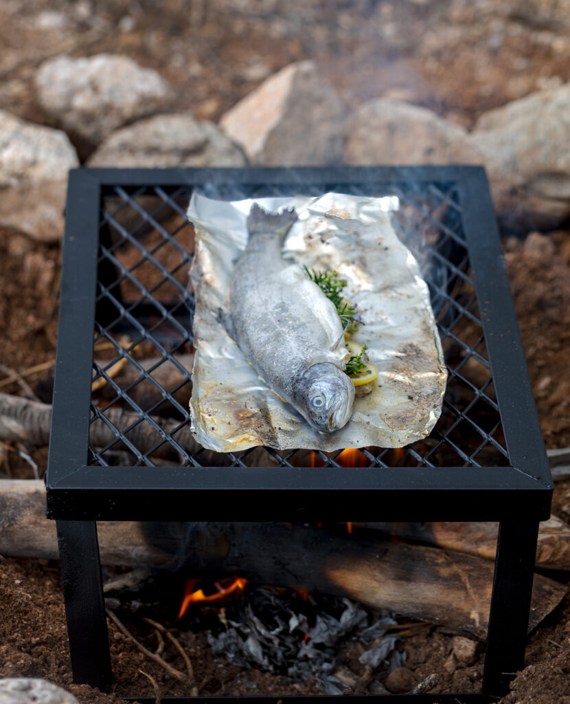 whole trout grilling on a camp stove over a wood campfire. Recipe and photo by Jackie Alpers.